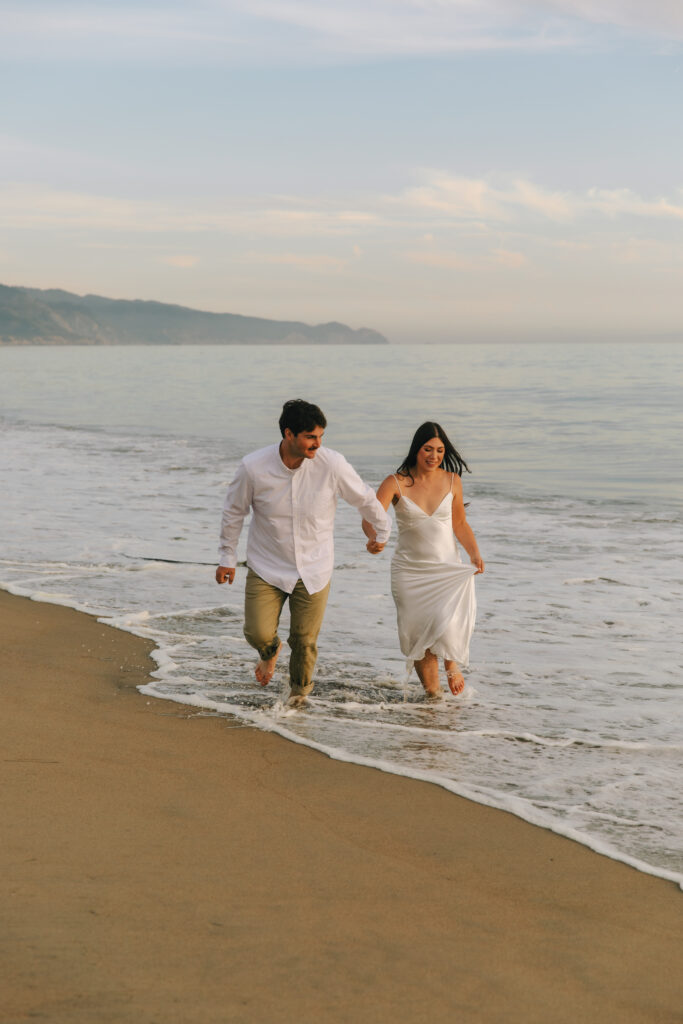 Couple running on the beach during their engagement photo session in Point Reyes California. 