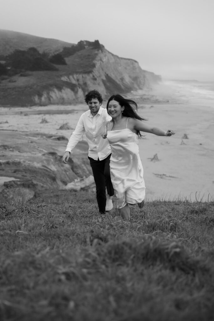 Couple running on Half Moon Bay beach cliffs, Bay Area engagement photographer Rose Freedman