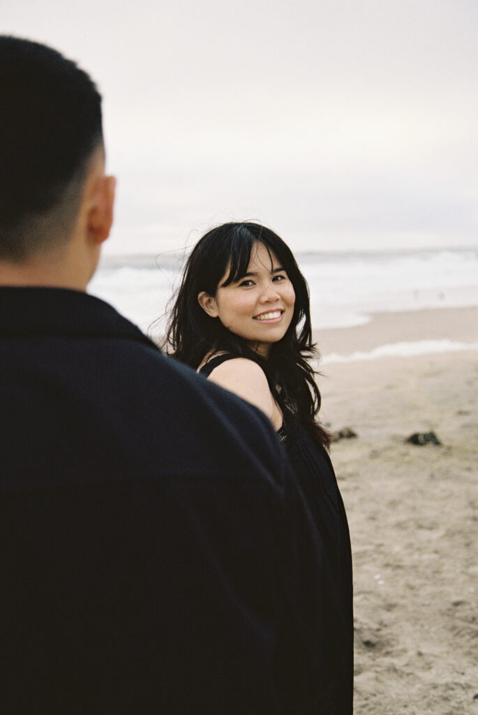 Woman smiling at camera on Half Moon Bay beach on 35mm film, Bay Area couples photographer Rose Freedman