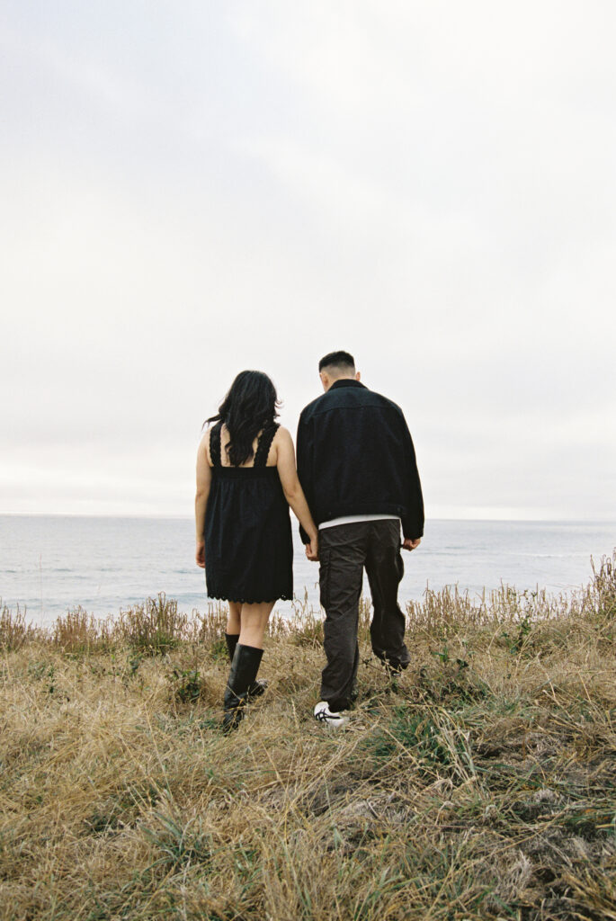 Couple walking through golden coastal grass toward Half Moon Bay on 35mm film, Bay Area photographer Rose Freedman