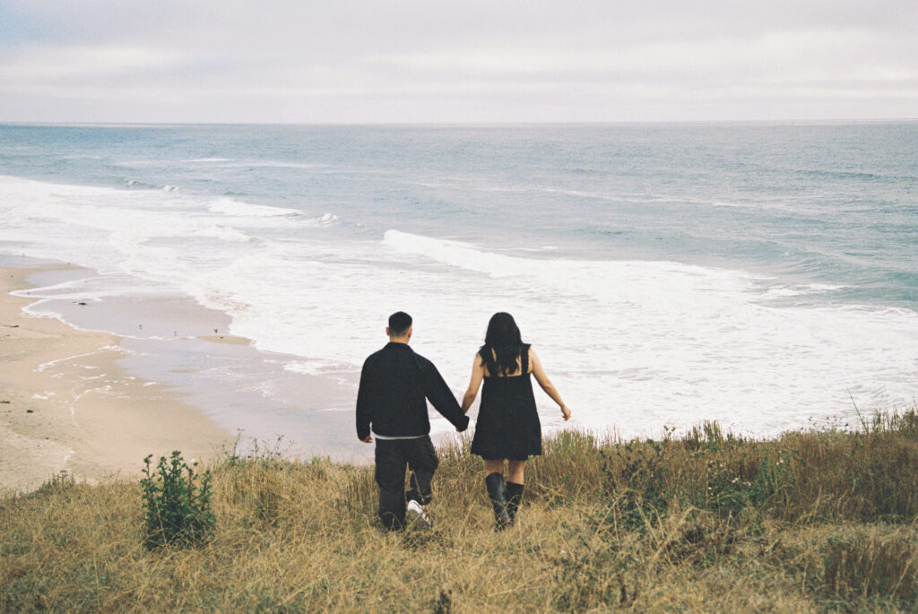 Couple walking down coastal hillside toward Half Moon Bay beach on 35mm film, Rose Freedman Photography