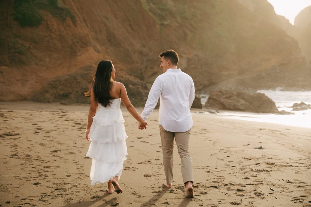 Couple walking hand in hand on Rodeo Beach at golden hour, Bay Area engagement photographer Rose Freedman