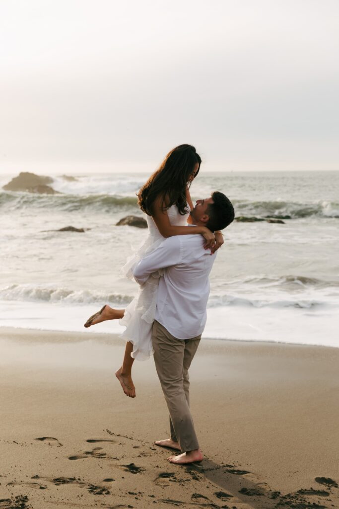 Man lifting woman on Rodeo Beach engagement session, Bay Area engagement photographer Rose Freedman