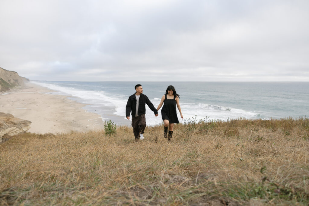 Couple running toward camera on Half Moon Bay bluff, Bay Area couples photographer Rose Freedman