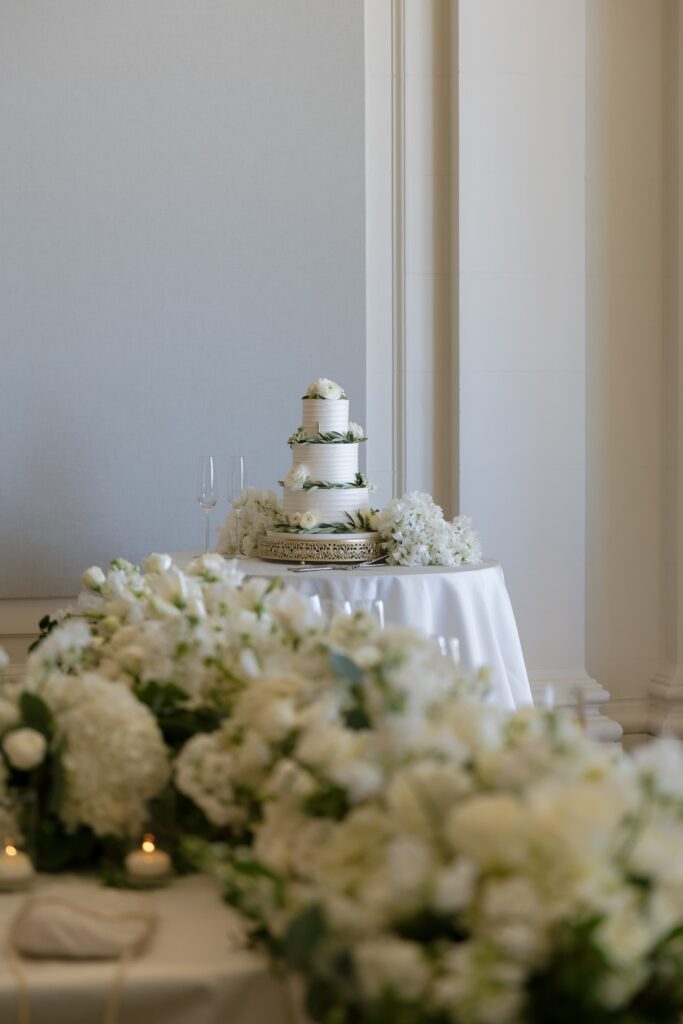 Three-tier wedding cake surrounded by white floral arrangements at Flood Mansion reception, San Francisco wedding photographer Rose Freedman
