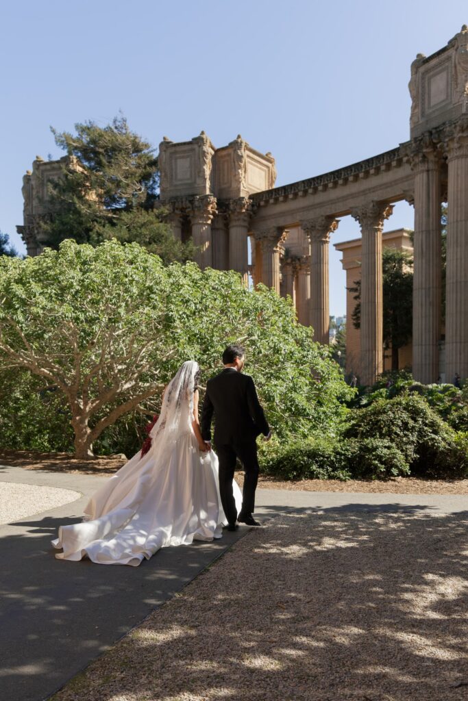 Bride and groom walking toward Palace of Fine Arts colonnade with cathedral train, San Francisco wedding photographer Rose Freedman