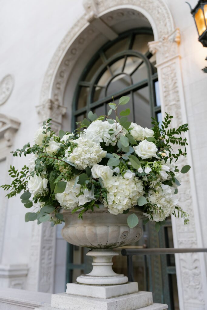 White hydrangea and rose floral arrangement in stone urn at Flood Mansion entrance, San Francisco wedding photographer Rose Freedman