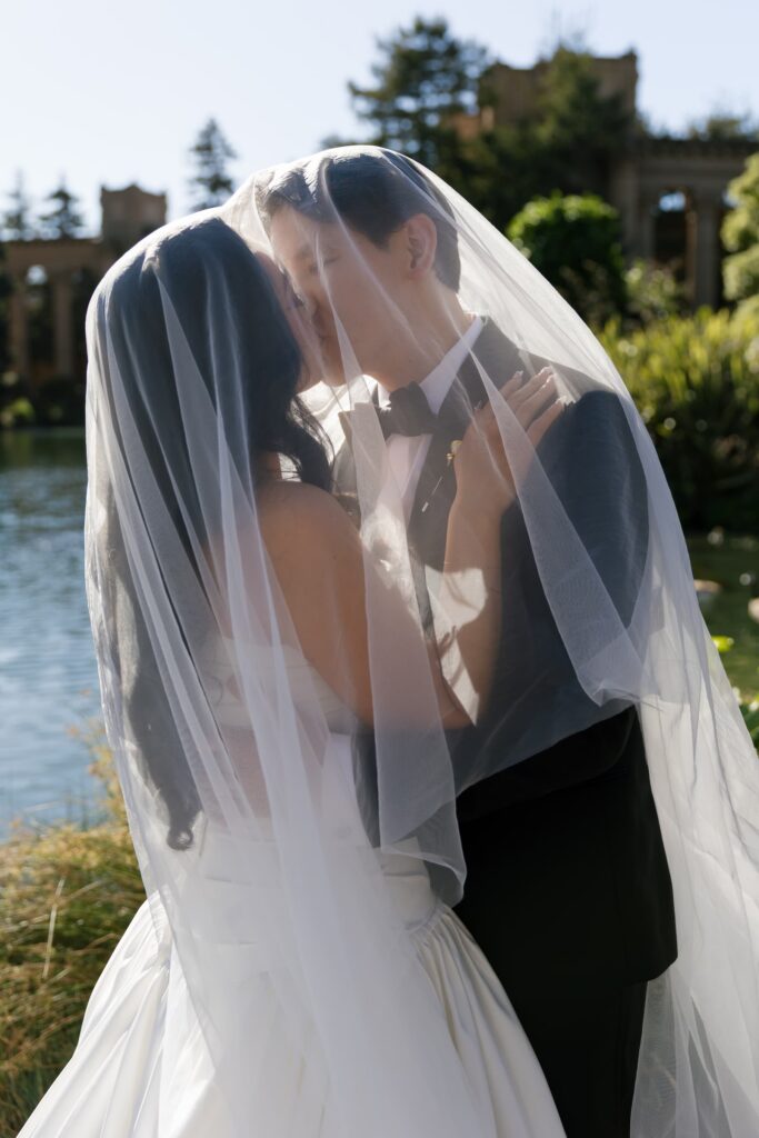 Bride and groom kissing under veil at Palace of Fine Arts lagoon, San Francisco wedding photographer Rose Freedman