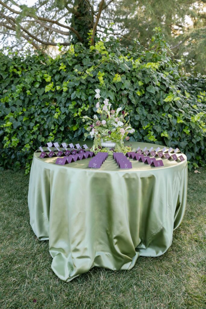 Purple escort card display on sage linen table against ivy wall at Park Winters wedding, Rose Freedman Photography