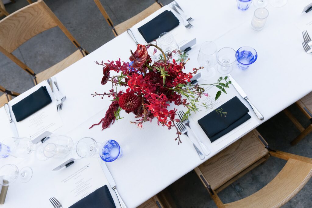 Aerial view of wedding reception table setting with burgundy florals and blue glasses at Foreign Cinema, Rose Freedman Photography