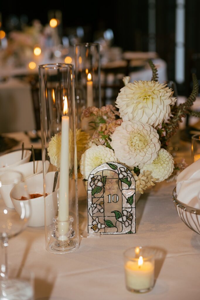 Stained glass arch table number with white dahlia centerpiece and candles at Kohl Mansion wedding, Bay Area wedding photographer