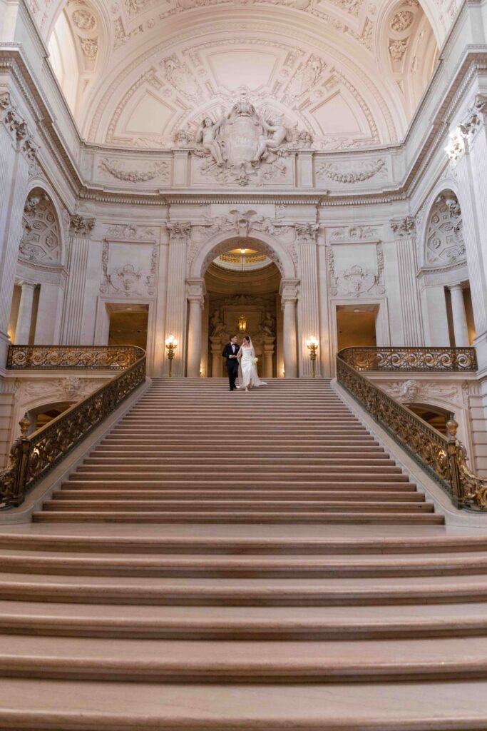 Bride and groom on grand staircase at SF City Hall showing ornate Beaux-Arts architecture, San Francisco wedding photographer Rose Freedman