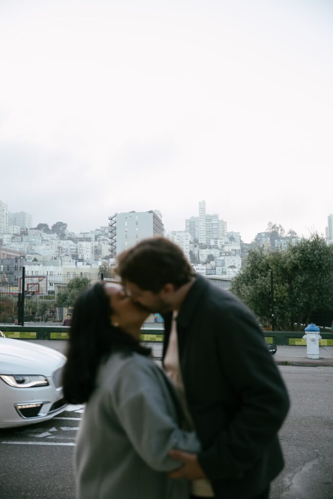 Couple kissing with San Francisco cityscape in background, urban engagement photographer Rose Freedman