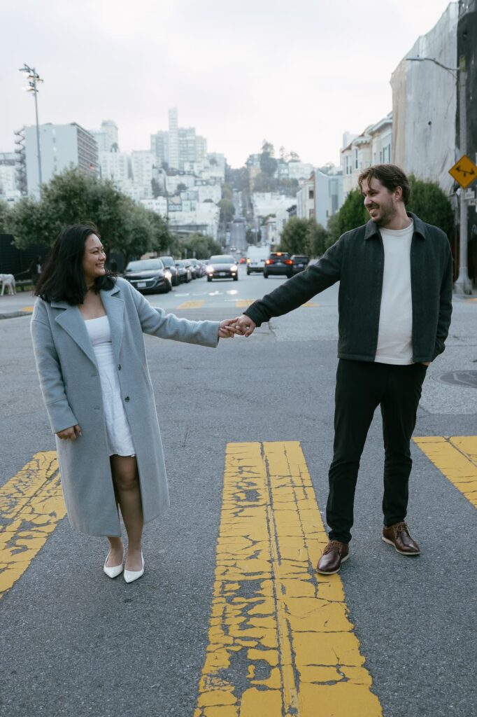 Couple holding hands laughing on San Francisco hill street, Bay Area engagement photographer Rose Freedman