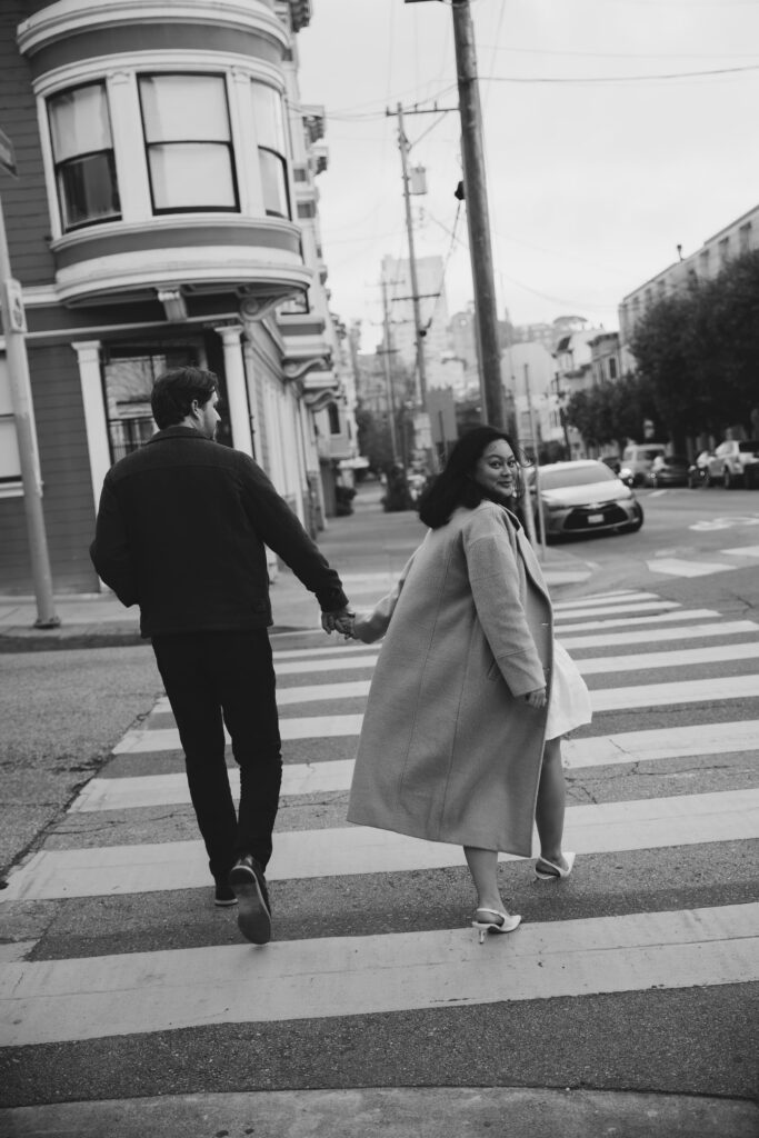 Couple walking hand in hand across San Francisco crosswalk, Bay Area engagement photographer Rose Freedman