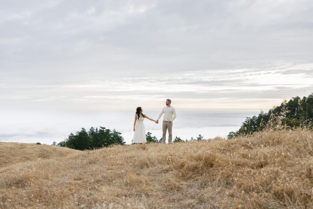 Couple holding hands on Mount Tamalpais hilltop above fog layer, Bay Area engagement photographer Rose Freedman