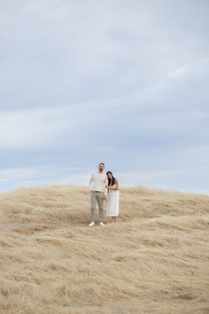 Couple standing together on Mount Tamalpais hilltop against cloudy sky, Bay Area engagement photographer Rose Freedman