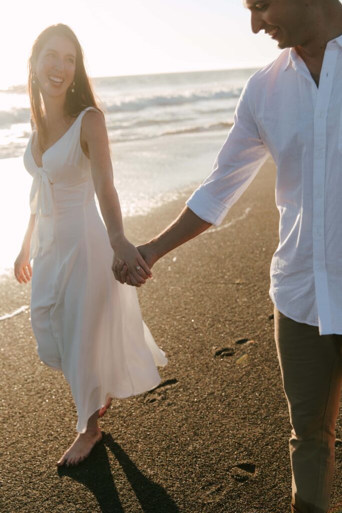 Couple walking on beach at golden hour engagement session, white sundress, Bay Area engagement photographer Rose Freedman