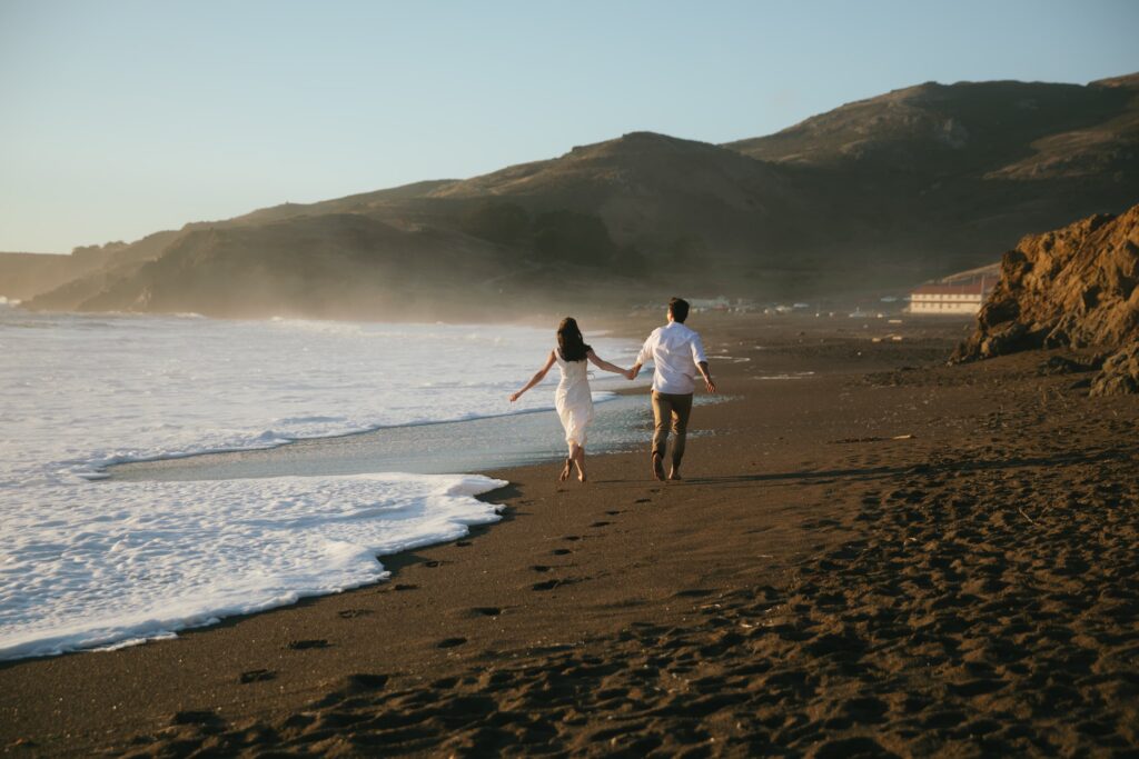 Couple running on beach at golden hour engagement session, white sundress, Bay Area engagement photographer Rose Freedman