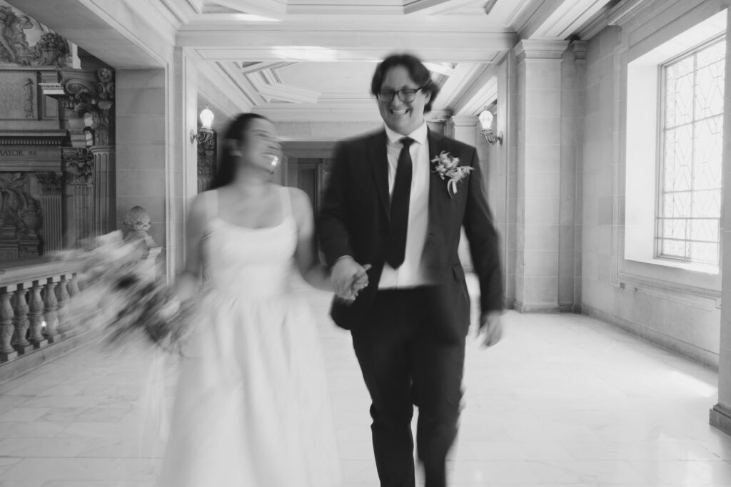 Couple laughing and running through San Francisco City Hall hallway, elopement photographer Rose Freedman