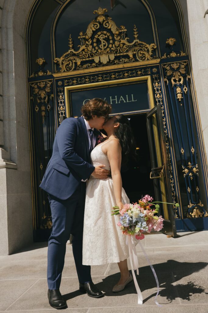 Couple kissing in front of San Francisco City Hall ornate door with colorful bouquet, Rose Freedman Photography
