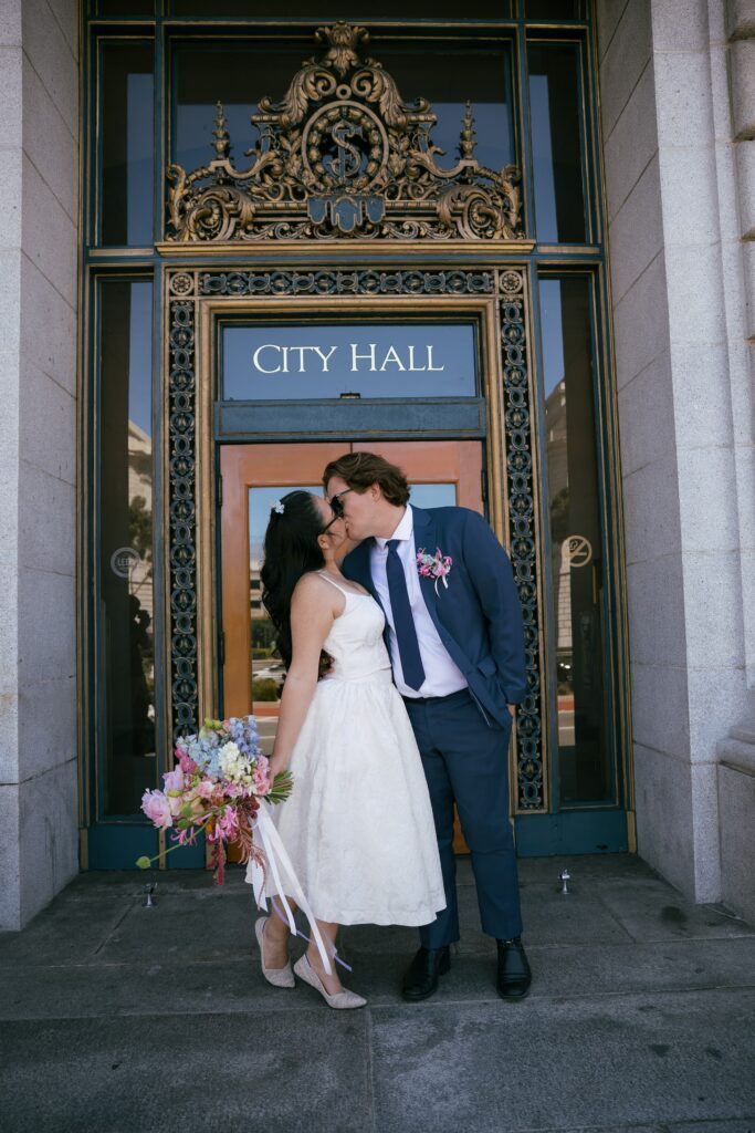 Couple kissing in front of San Francisco City Hall door with bouquet, elopement photographer Rose Freedman