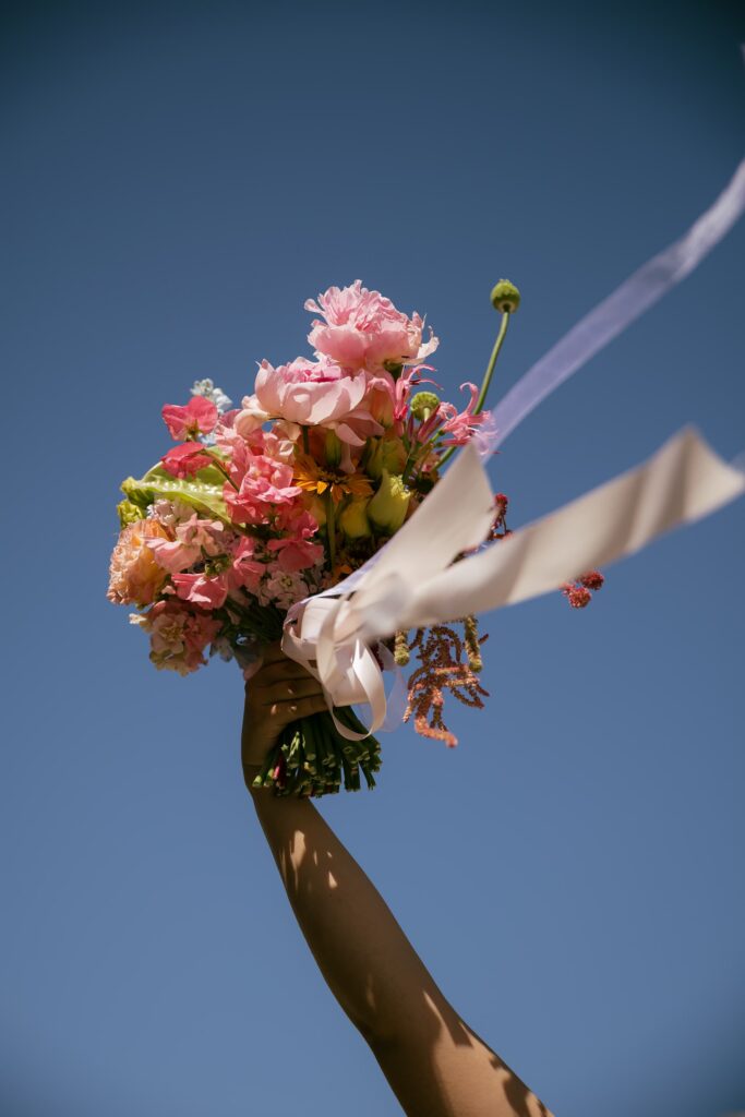 Colorful wedding bouquet raised against blue sky San Francisco City Hall elopement, Rose Freedman Photography