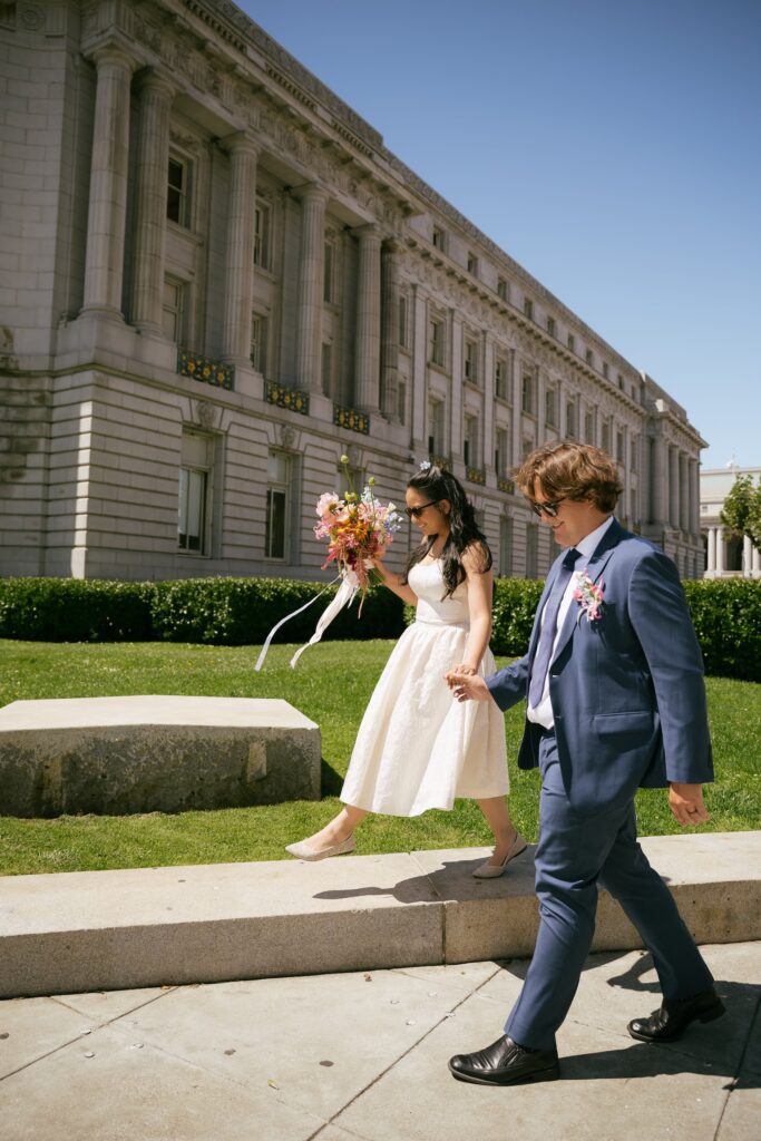 Couple walking hand in hand outside San Francisco City Hall, elopement photographer Rose Freedman