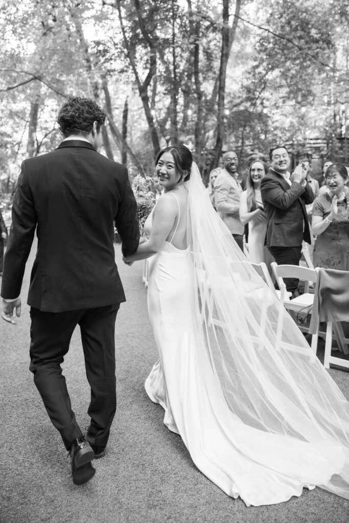 Bride and groom walking away after their ceremony at Saratoga Springs redwood wedding, cathedral length veil trailing behind