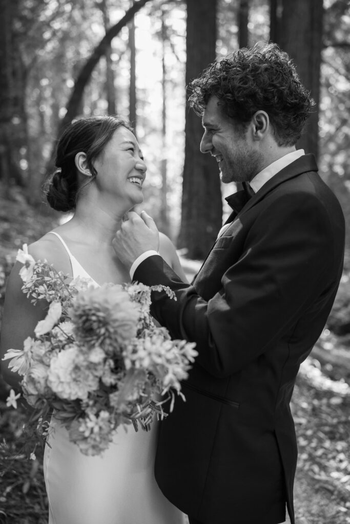 Black and white photo of bride and groom smiling at each other among redwood trees at Saratoga Springs wedding